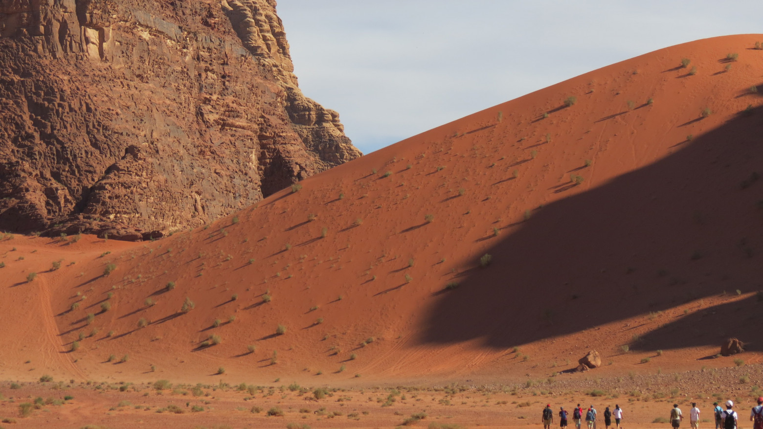 A amber sand dune towers over the tiny figures of a group of people.